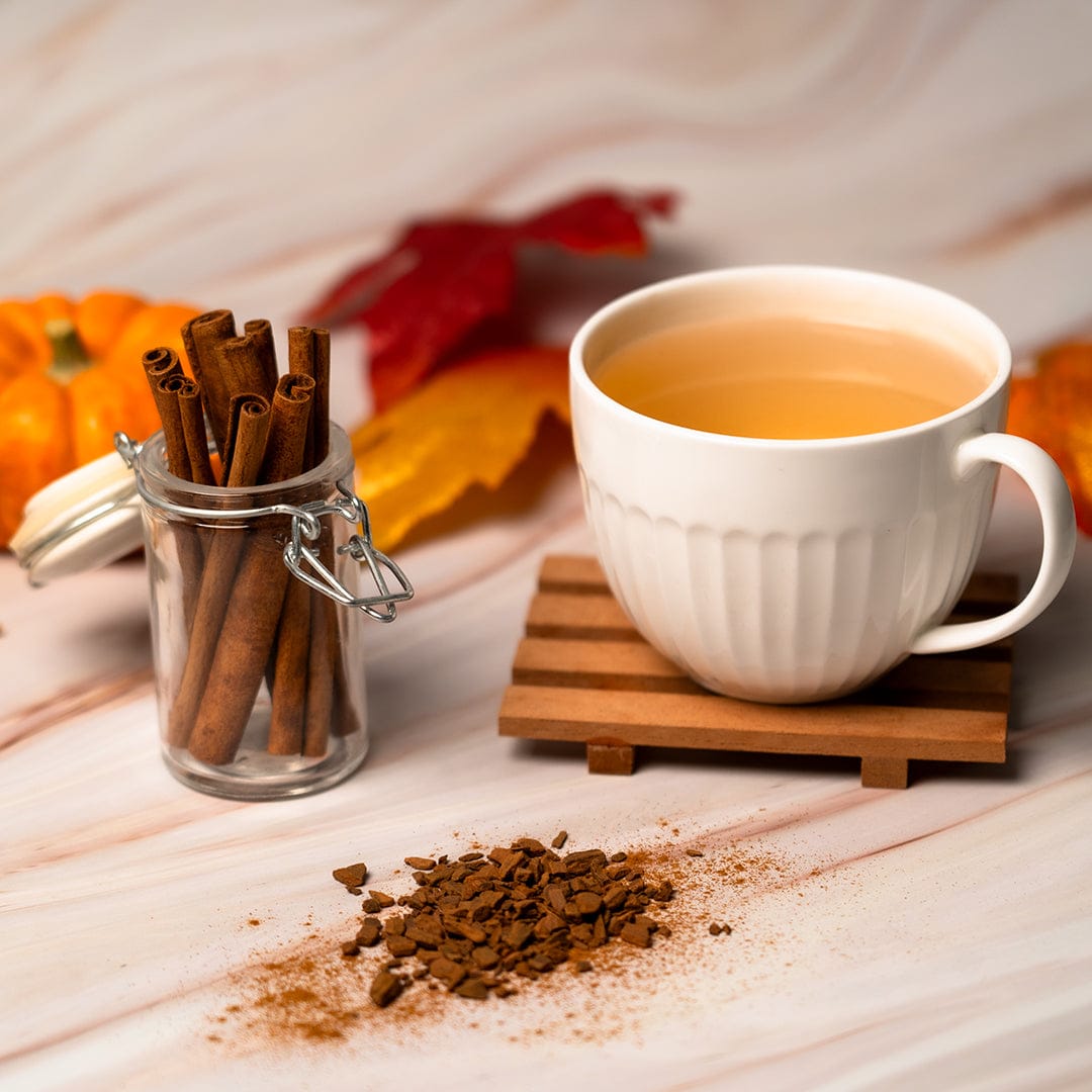 White mug of cinnamon tea with sticks, ground cinnamon and autumn decor
