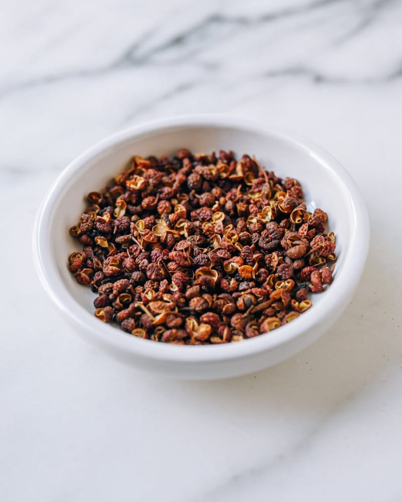 White bowl filled with dried red Sichuan peppercorns on a marble surface