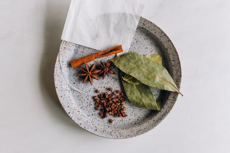 Cinnamon, star anise, bay leaves and Sichuan peppercorns on a plate with a spice sachet