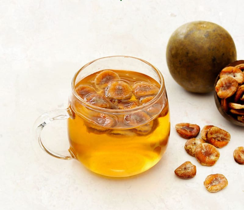 Golden monk fruit tea in a glass mug beside whole fruit and dried slices