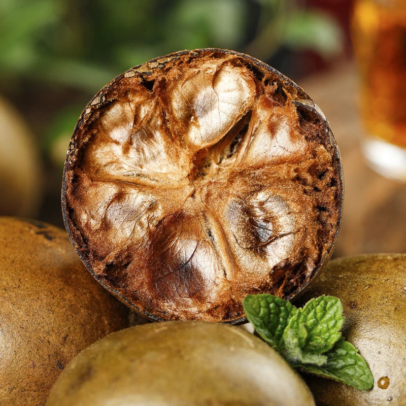 A monk fruit cut open showing fibrous pulp beside whole fruits and mint leaves
