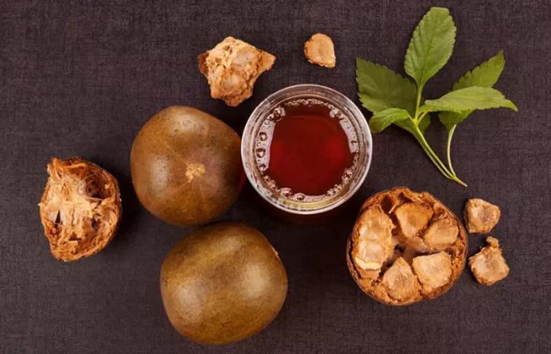 Glass of amber monk fruit tea with whole and broken dried fruit beside it