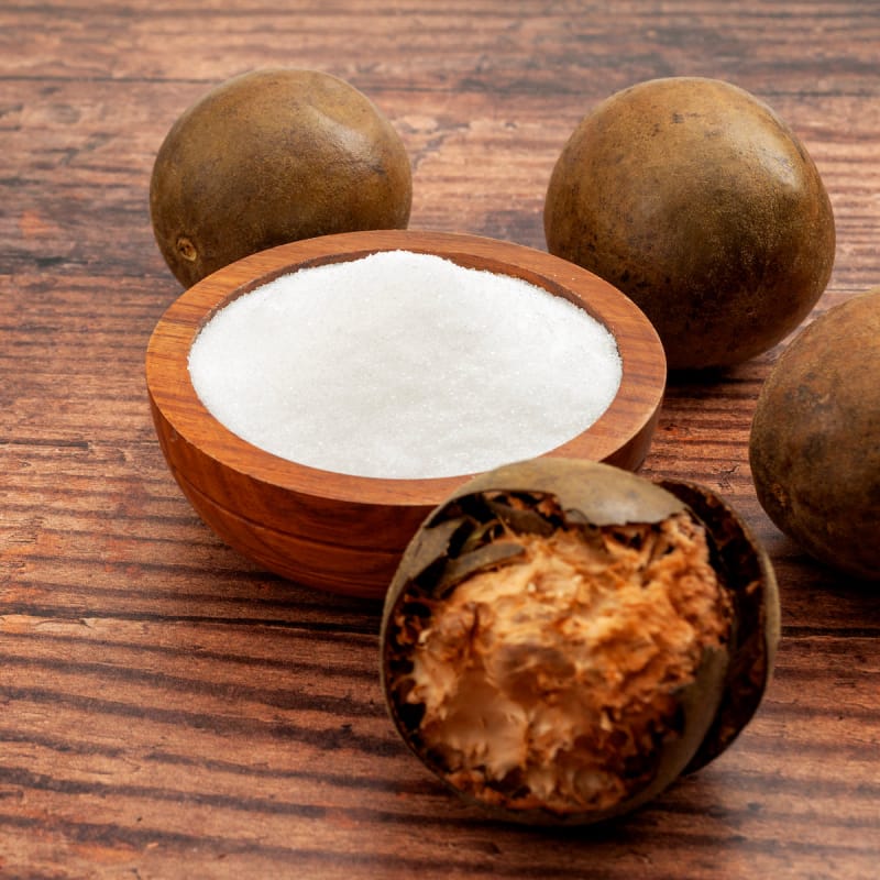 Wooden bowl of white monk fruit extract powder surrounded by whole and broken fruit