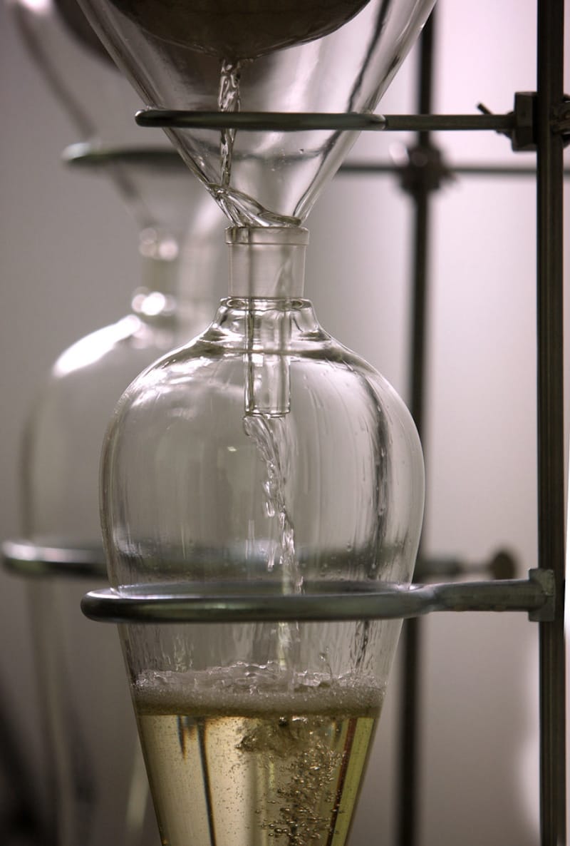 Separatory funnel extraction in a laboratory with yellow liquid dripping into a flask