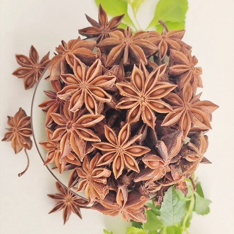 Heap of dried star anise pods on a white surface with green leaves