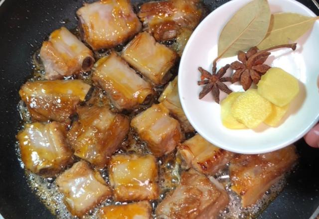 Braised ribs in a wok with star anise, bay leaves and ginger in a small dish beside