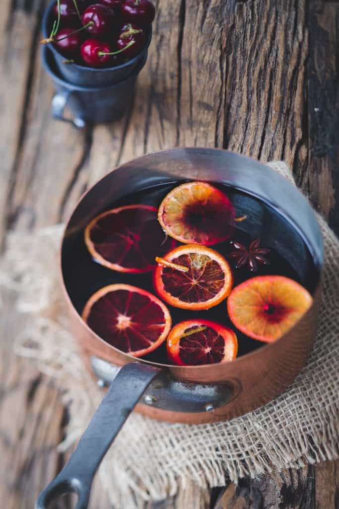 Copper pot of mulled wine with blood orange slices and star anise on a rustic table